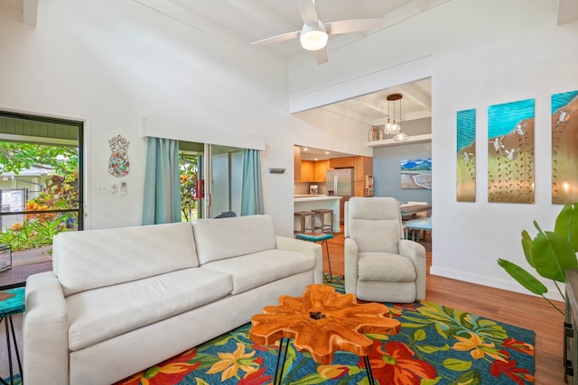 living room with a high ceiling, beamed ceiling, hardwood / wood-style flooring, and ceiling fan