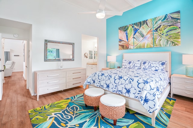 bedroom with light hardwood / wood-style floors, beamed ceiling, ceiling fan, and connected bathroom