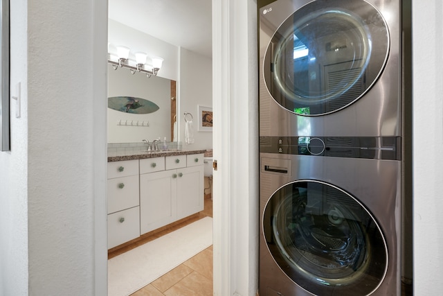 laundry area with light tile patterned flooring, sink, and stacked washer / dryer