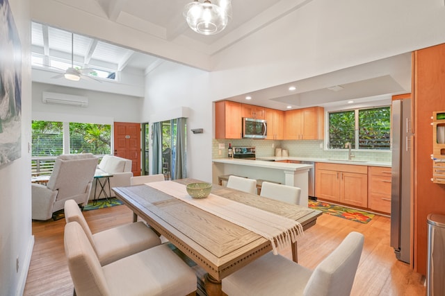 dining room with a wealth of natural light, sink, a wall mounted air conditioner, ceiling fan, and light hardwood / wood-style flooring