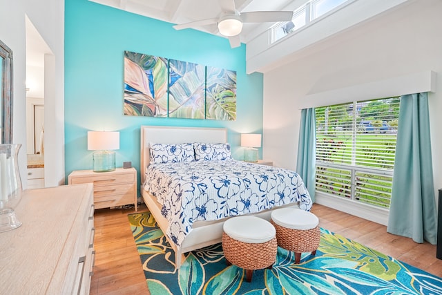 bedroom featuring beamed ceiling, a towering ceiling, ceiling fan, and light wood-type flooring