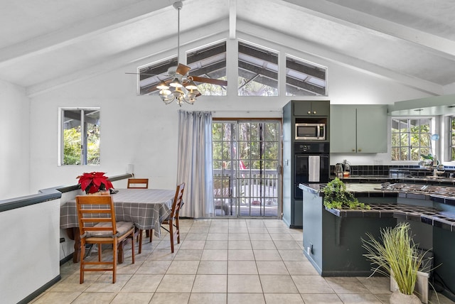 kitchen featuring a wealth of natural light, lofted ceiling with beams, light tile patterned floors, and stainless steel microwave