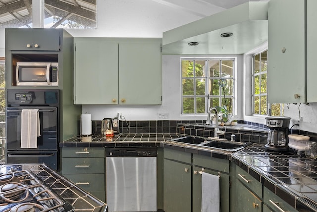 kitchen with stainless steel appliances, vaulted ceiling, sink, tile countertops, and green cabinets