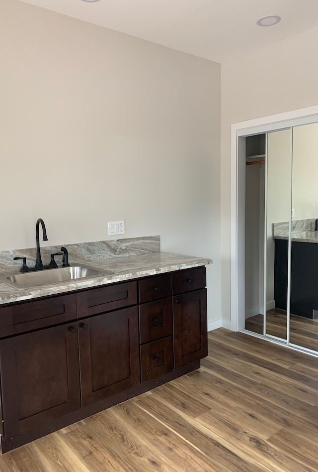 kitchen with dark brown cabinets, light hardwood / wood-style floors, light stone countertops, and sink