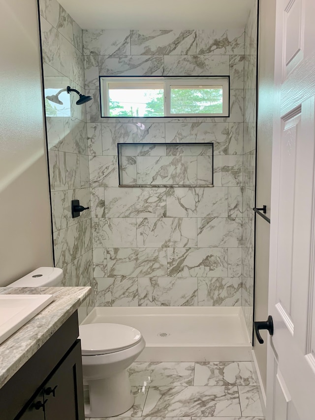 bathroom with a tile shower, vanity, and toilet