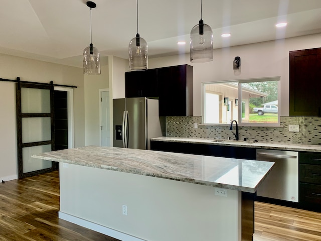 kitchen featuring light wood-type flooring, a barn door, stainless steel appliances, and sink