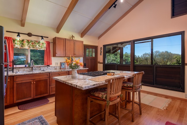 kitchen with sink, a kitchen island, light stone countertops, light wood-type flooring, and beam ceiling