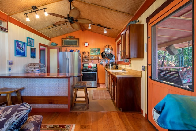 kitchen with appliances with stainless steel finishes, ceiling fan, wooden walls, light hardwood / wood-style flooring, and lofted ceiling