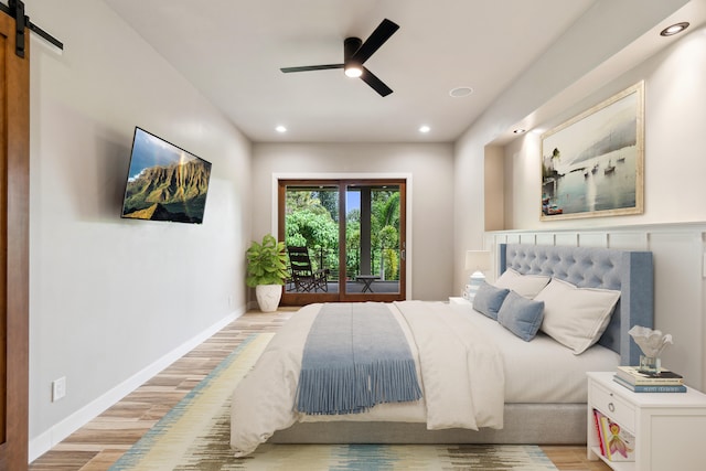 bedroom with a barn door, ceiling fan, and light hardwood / wood-style floors