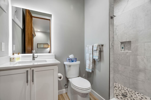 bathroom with tiled shower, hardwood / wood-style floors, vanity, and toilet