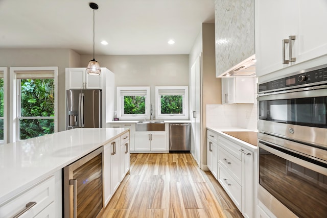 kitchen with appliances with stainless steel finishes, beverage cooler, sink, pendant lighting, and white cabinets