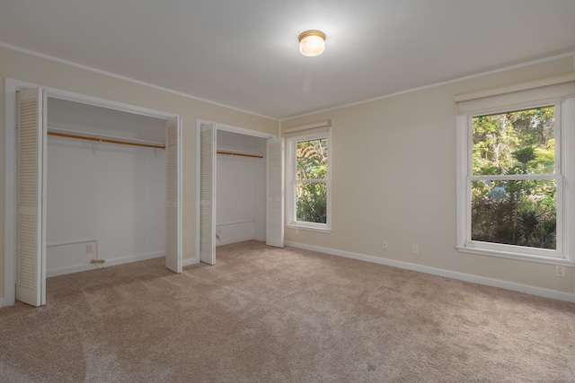 unfurnished bedroom featuring light colored carpet, crown molding, multiple windows, and multiple closets