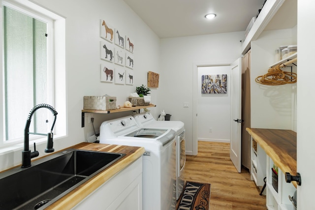 clothes washing area with light wood-type flooring, independent washer and dryer, and sink