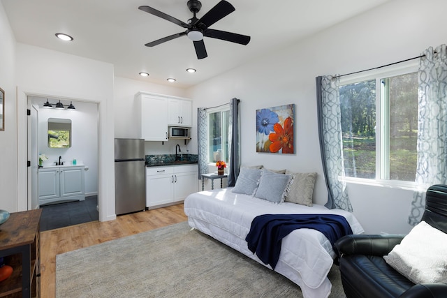 bedroom featuring stainless steel fridge, light hardwood / wood-style floors, ceiling fan, and sink