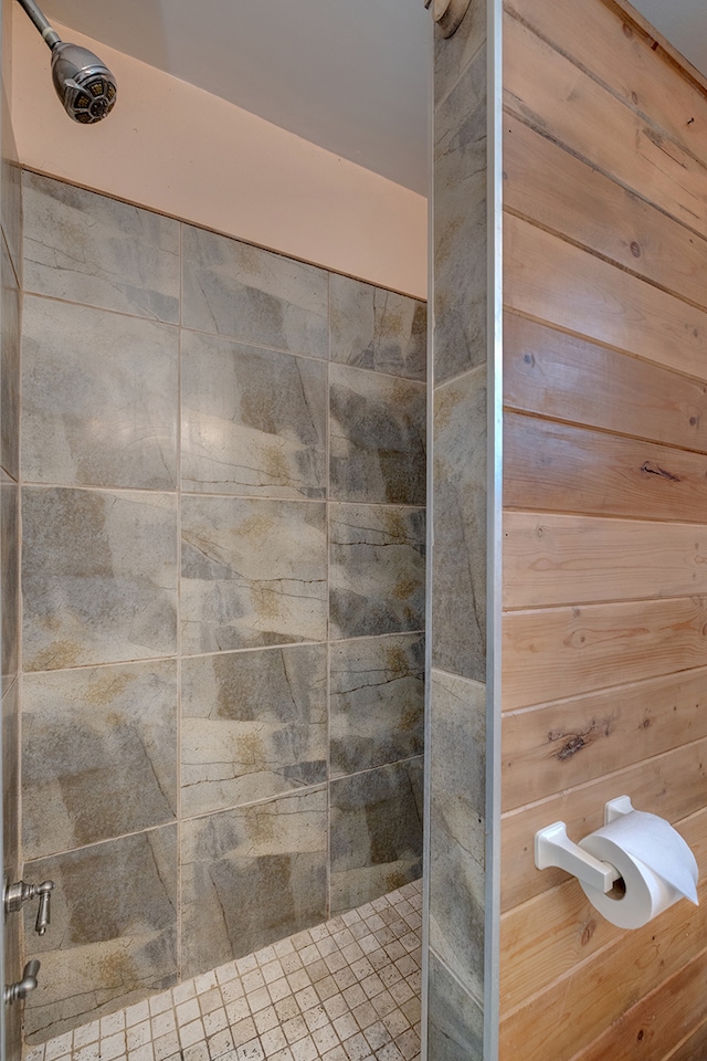 bathroom with tiled shower and wooden walls