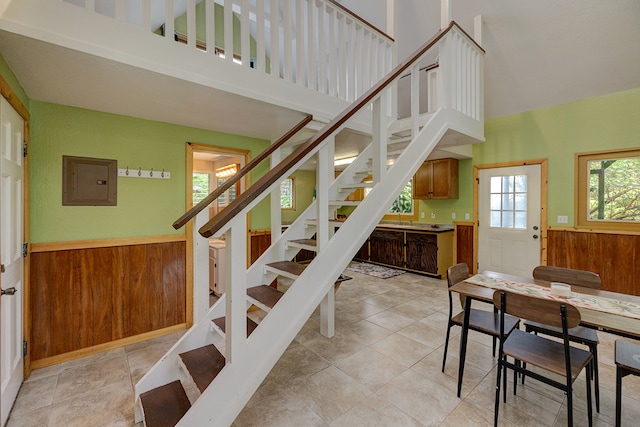 staircase featuring electric panel, wooden walls, and a high ceiling