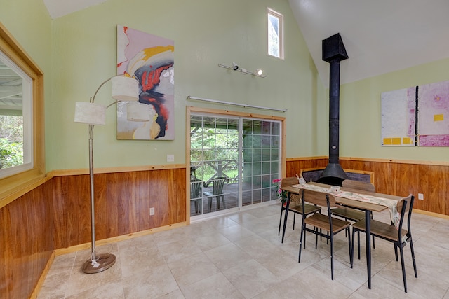 dining area featuring high vaulted ceiling, a wood stove, and wooden walls