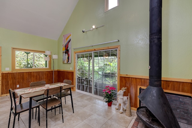 dining room with wood walls, light tile patterned flooring, a wood stove, and high vaulted ceiling