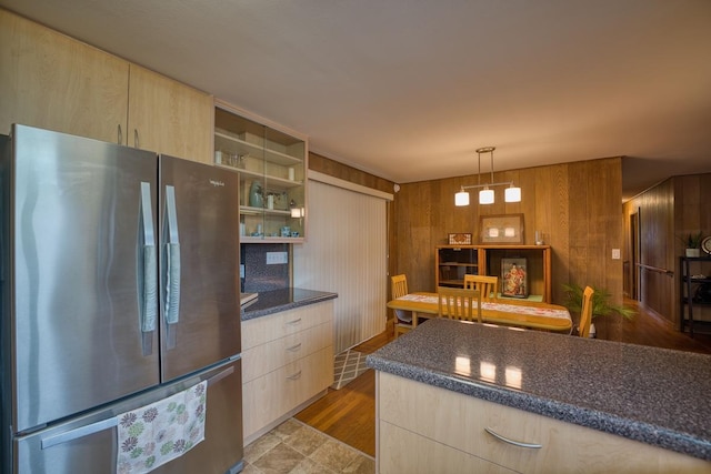 kitchen with wood walls, light brown cabinets, hanging light fixtures, light wood-type flooring, and stainless steel refrigerator