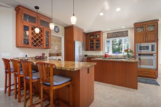 kitchen with kitchen peninsula, pendant lighting, vaulted ceiling, a kitchen bar, and appliances with stainless steel finishes