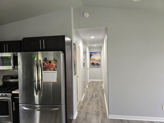 kitchen featuring dark cabinets, stainless steel appliances, vaulted ceiling, light countertops, and light wood-type flooring