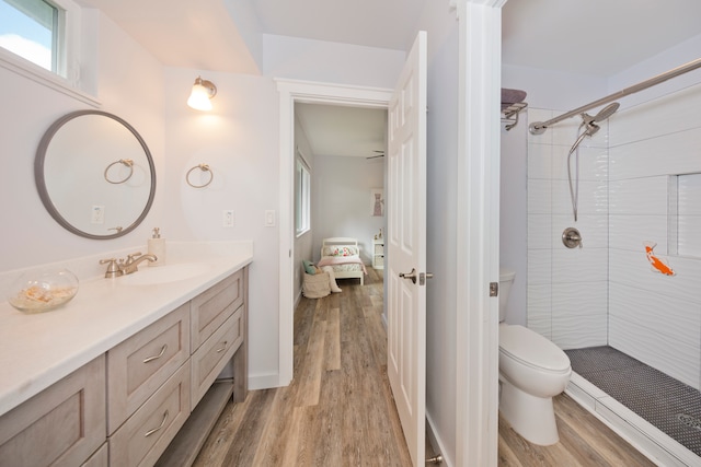 bathroom with a tile shower, vanity, wood-type flooring, and toilet