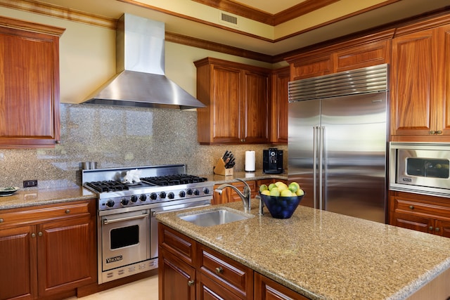 kitchen featuring a center island with sink, wall chimney range hood, sink, built in appliances, and ornamental molding