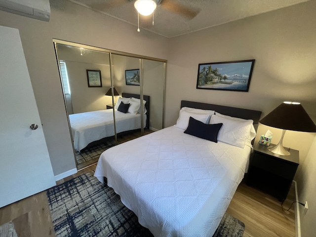 bedroom featuring an AC wall unit, ceiling fan, a textured ceiling, wood-type flooring, and a closet