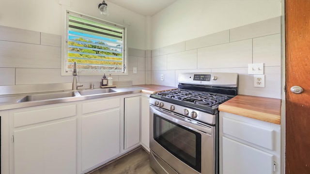 kitchen with tasteful backsplash, sink, stainless steel gas stove, butcher block countertops, and white cabinetry