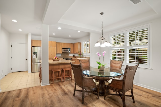 dining room featuring a chandelier, light wood-type flooring, and a tray ceiling