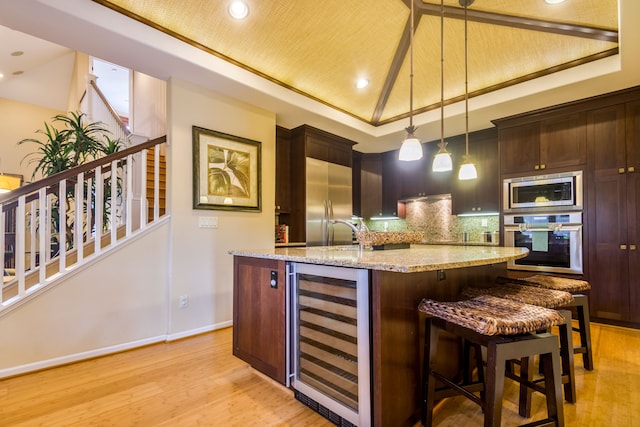 kitchen with a raised ceiling, light stone counters, hanging light fixtures, and beverage cooler