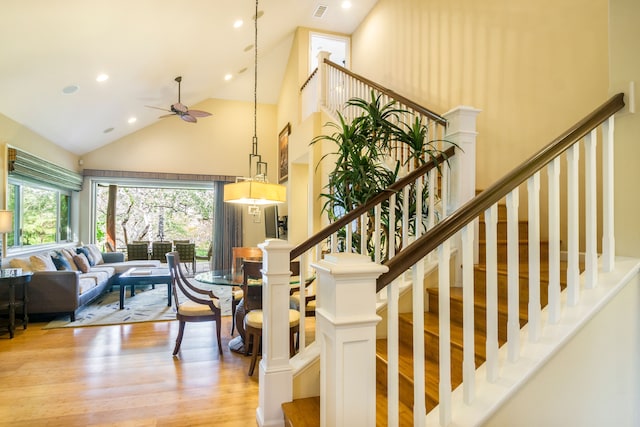 stairs with ceiling fan, high vaulted ceiling, and hardwood / wood-style flooring