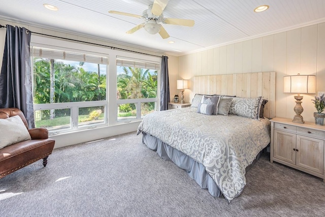 carpeted bedroom with wooden walls, ceiling fan, and crown molding