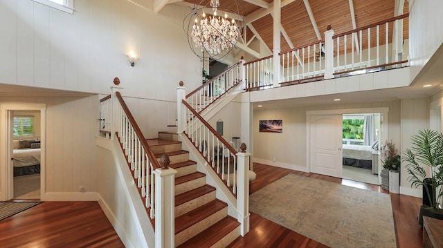 staircase with a notable chandelier, beam ceiling, wood-type flooring, and high vaulted ceiling