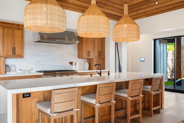 kitchen with wall chimney range hood, stainless steel stove, light tile patterned floors, tasteful backsplash, and a breakfast bar area