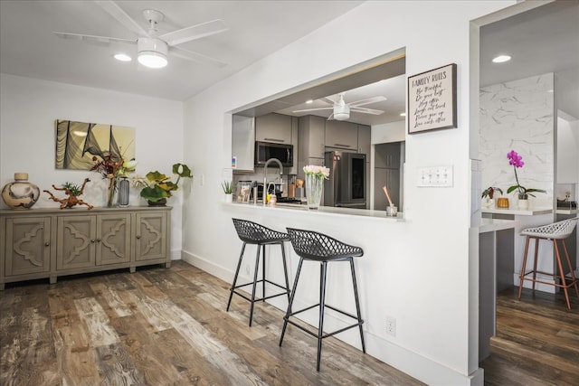 kitchen with ceiling fan, dark wood-type flooring, stainless steel appliances, a kitchen breakfast bar, and gray cabinets