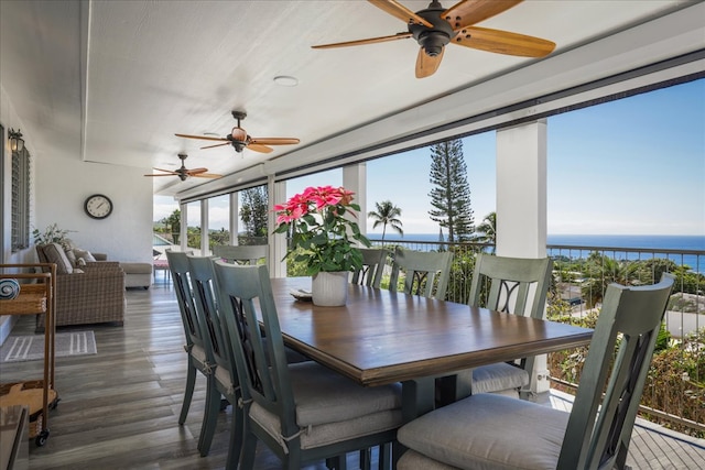 dining room featuring ceiling fan, dark hardwood / wood-style flooring, a water view, and a healthy amount of sunlight