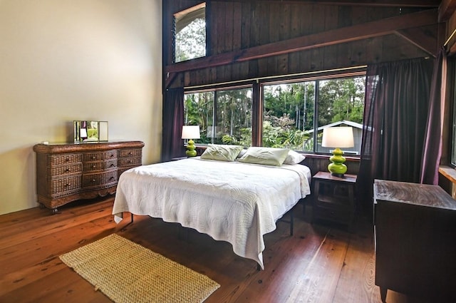 bedroom featuring dark hardwood / wood-style floors, wooden walls, and multiple windows