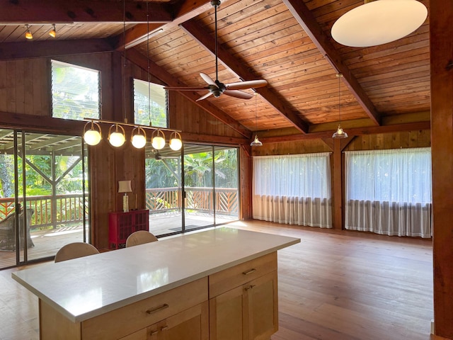 kitchen with vaulted ceiling with beams, wood walls, a center island, and light wood-type flooring