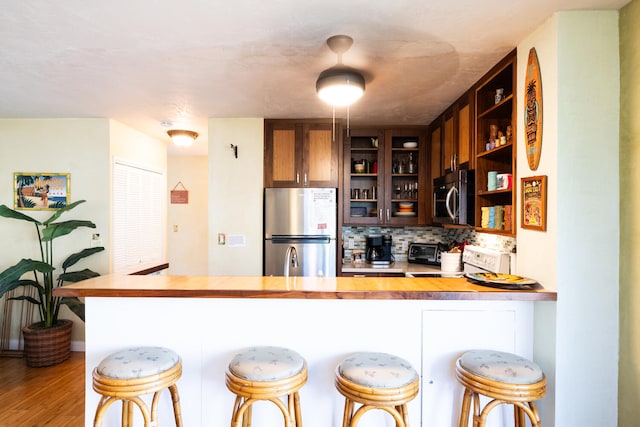 kitchen featuring stainless steel appliances, a kitchen breakfast bar, backsplash, kitchen peninsula, and hardwood / wood-style flooring