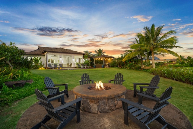 patio terrace at dusk featuring a gazebo, a fire pit, and a lawn