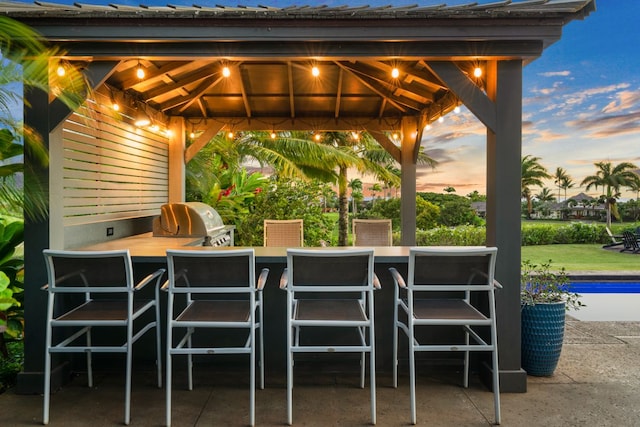 patio terrace at dusk featuring an outdoor bar, a gazebo, area for grilling, and exterior kitchen