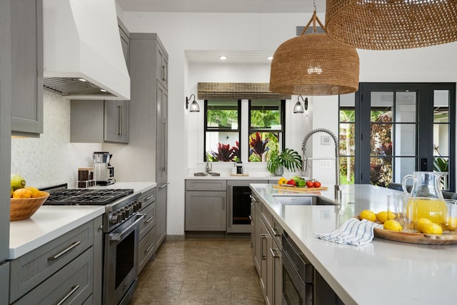 kitchen with sink, gray cabinets, high end range, decorative light fixtures, and custom exhaust hood