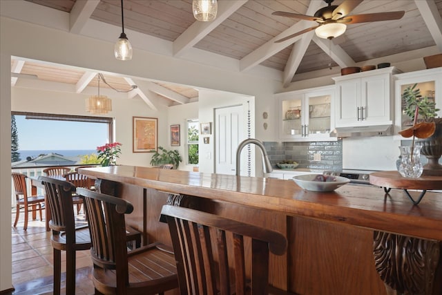 kitchen featuring vaulted ceiling with beams, tasteful backsplash, decorative light fixtures, white cabinetry, and butcher block counters