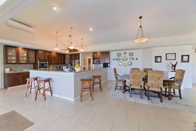 kitchen featuring tasteful backsplash, a kitchen breakfast bar, a wall mounted AC, light tile patterned floors, and appliances with stainless steel finishes