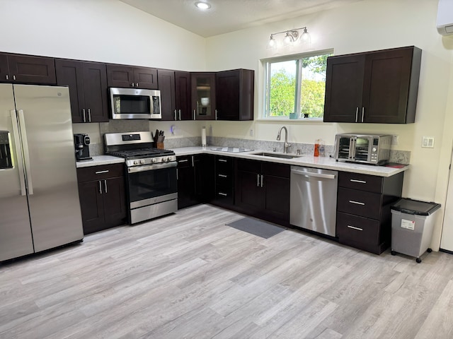 kitchen featuring light wood-type flooring, stainless steel appliances, sink, an AC wall unit, and lofted ceiling