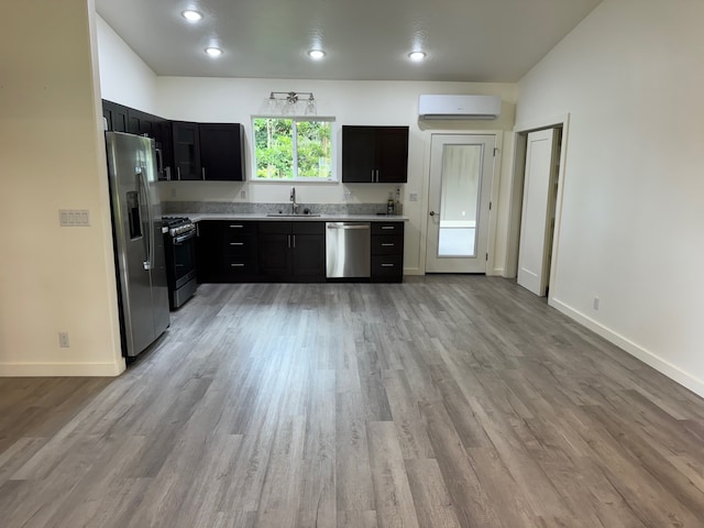 kitchen featuring a wall unit AC, sink, light hardwood / wood-style floors, and appliances with stainless steel finishes