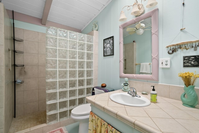 bathroom with ceiling fan, toilet, vanity, and tiled shower