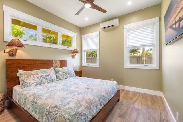 bedroom with hardwood / wood-style floors, ceiling fan, a wall unit AC, and multiple windows