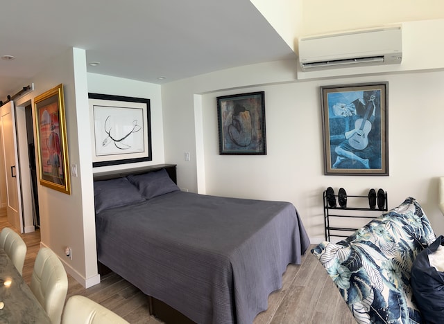 bedroom featuring a wall mounted air conditioner, a barn door, and light wood-type flooring